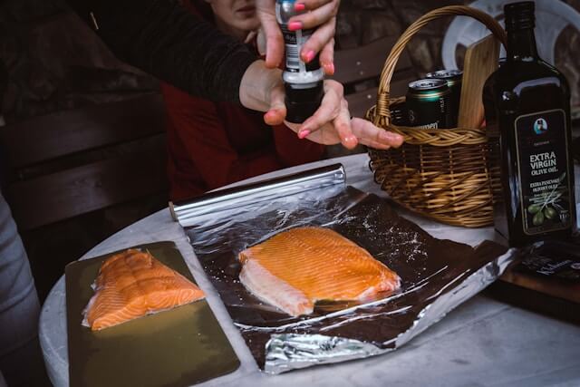 Adding seasoning to salmon fillet on foil with olive oil and basket.